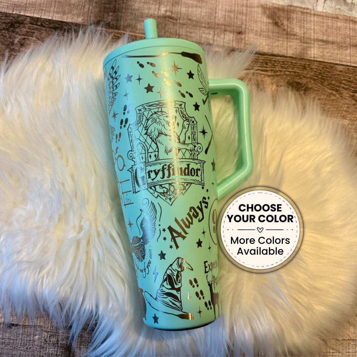 A turquoise tumbler mug with a handle and a small circular sticker on a white fur surface.