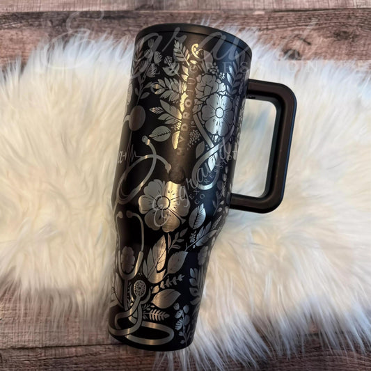 A black and silver insulated tumbler mug with a handle, placed on a white furry surface.