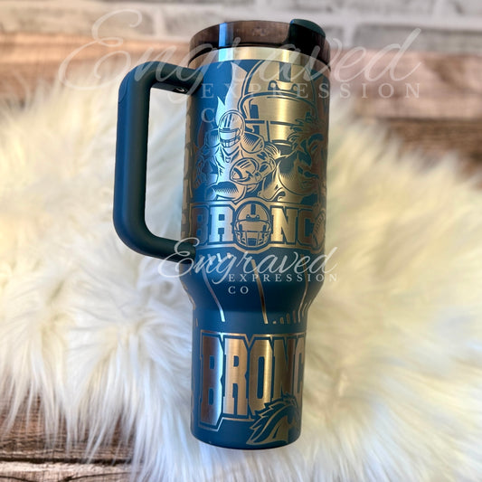 A blue and gold insulated travel mug with the word "BRONX" printed on it, sitting on a white furry surface.