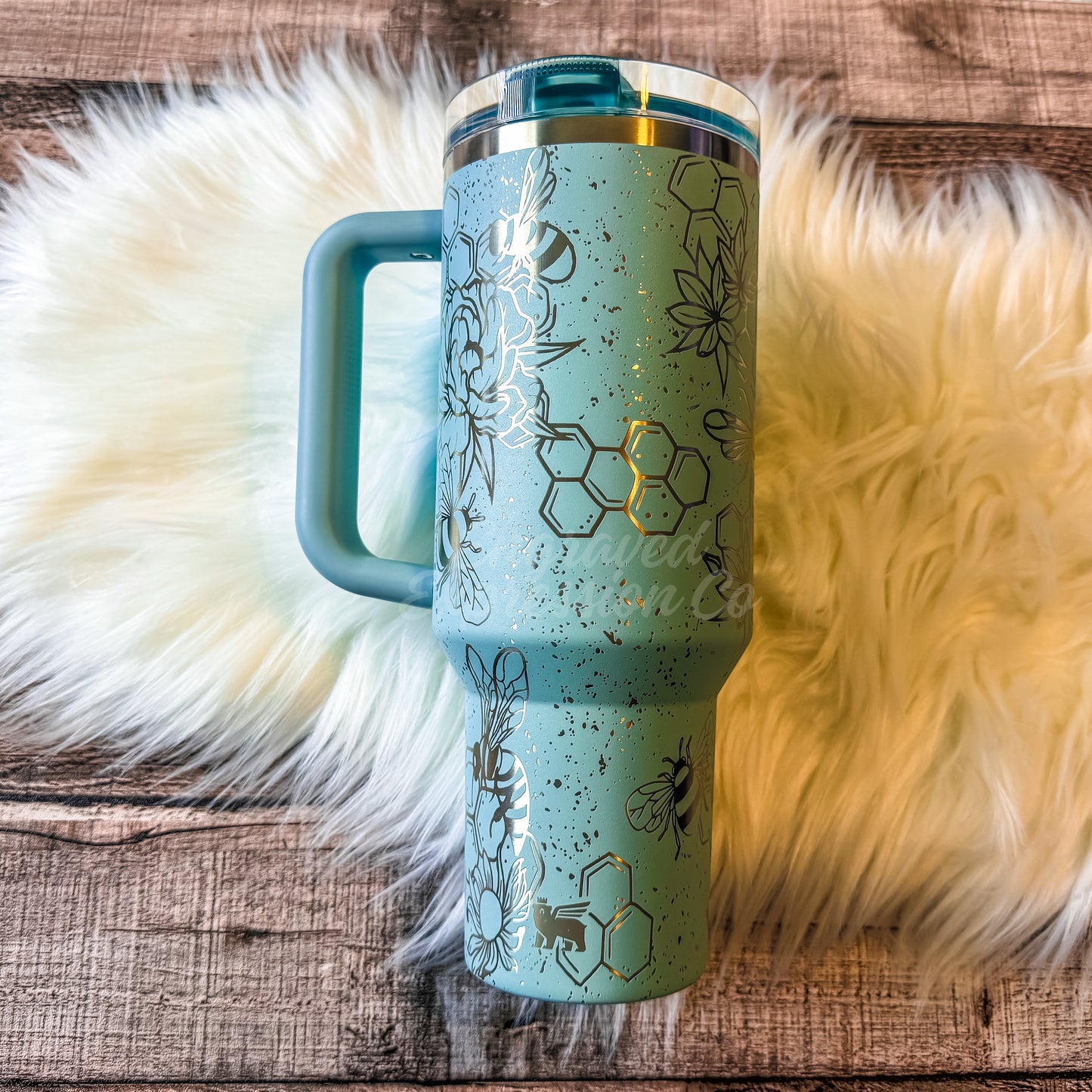 A turquoise insulated tumbler mug with a handle and lid, placed on a white furry surface.