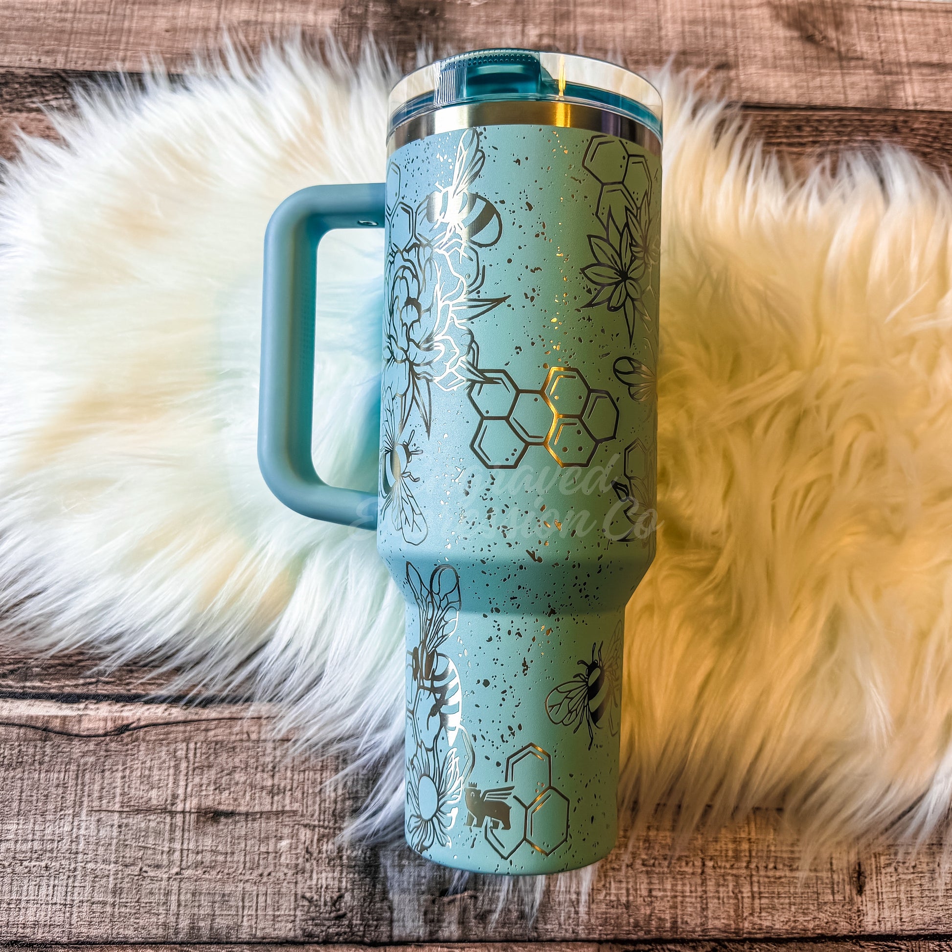 A turquoise insulated tumbler mug with a handle and lid, placed on a white furry surface.