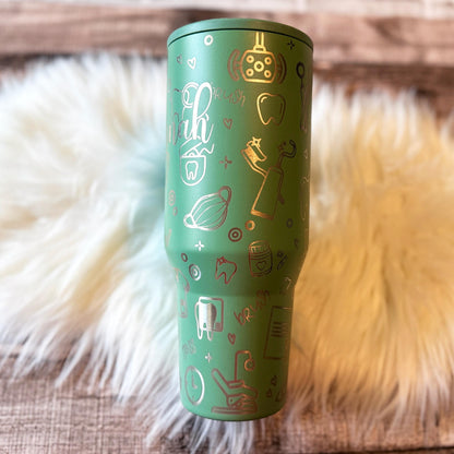 A green tumbler mug with various dental-related icons and text printed on it, placed on a white fur surface.