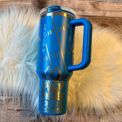 A blue Stanley sports thermos with a handle, featuring a design of a baseball and the text "Detroit" printed on it, placed on a white fur surface.