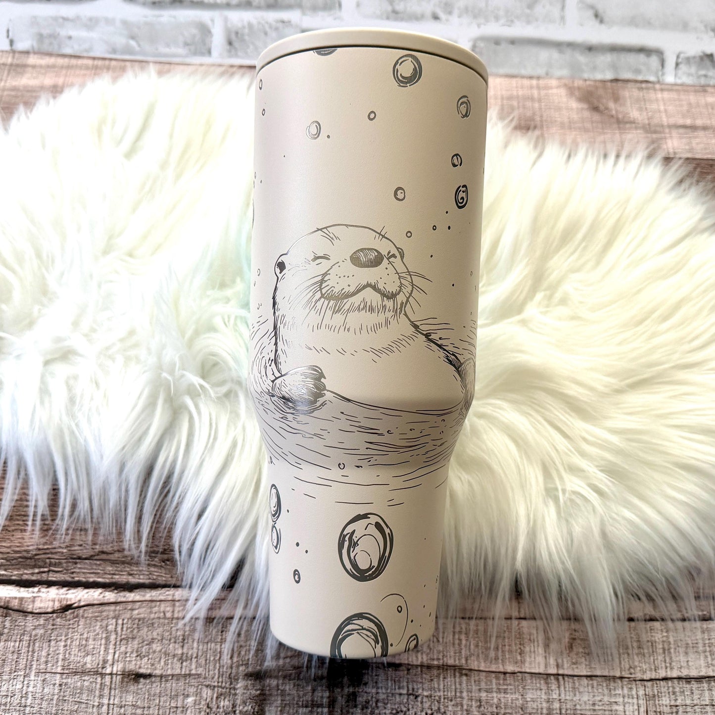 A white ceramic mug with a black and white illustration of an otter or seal on it, placed on a white fur rug.