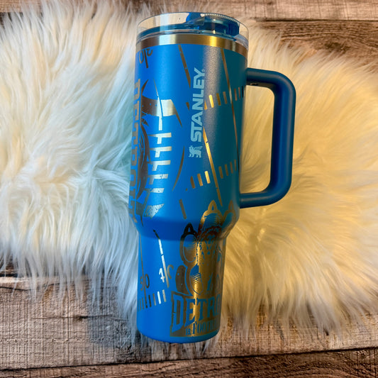 A blue insulated tumbler mug with a handle, placed on a white fur surface.