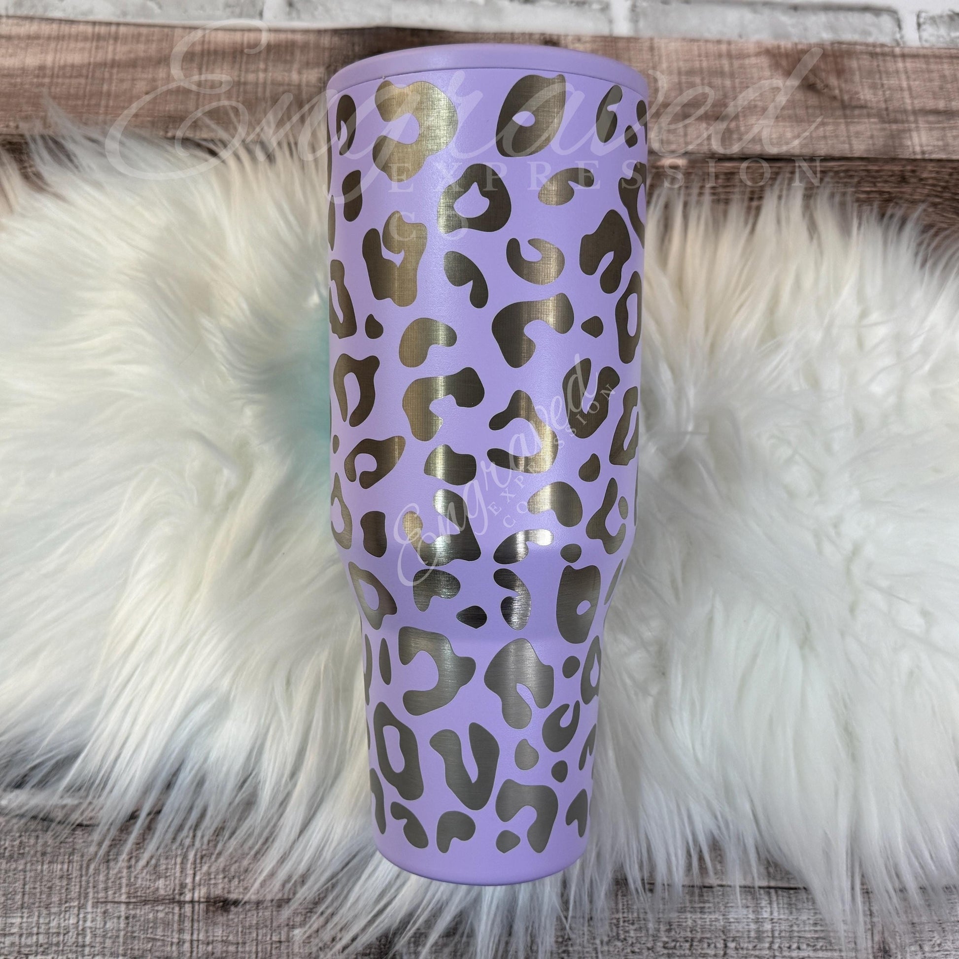 A purple leopard print tumbler sits on a white furry surface.