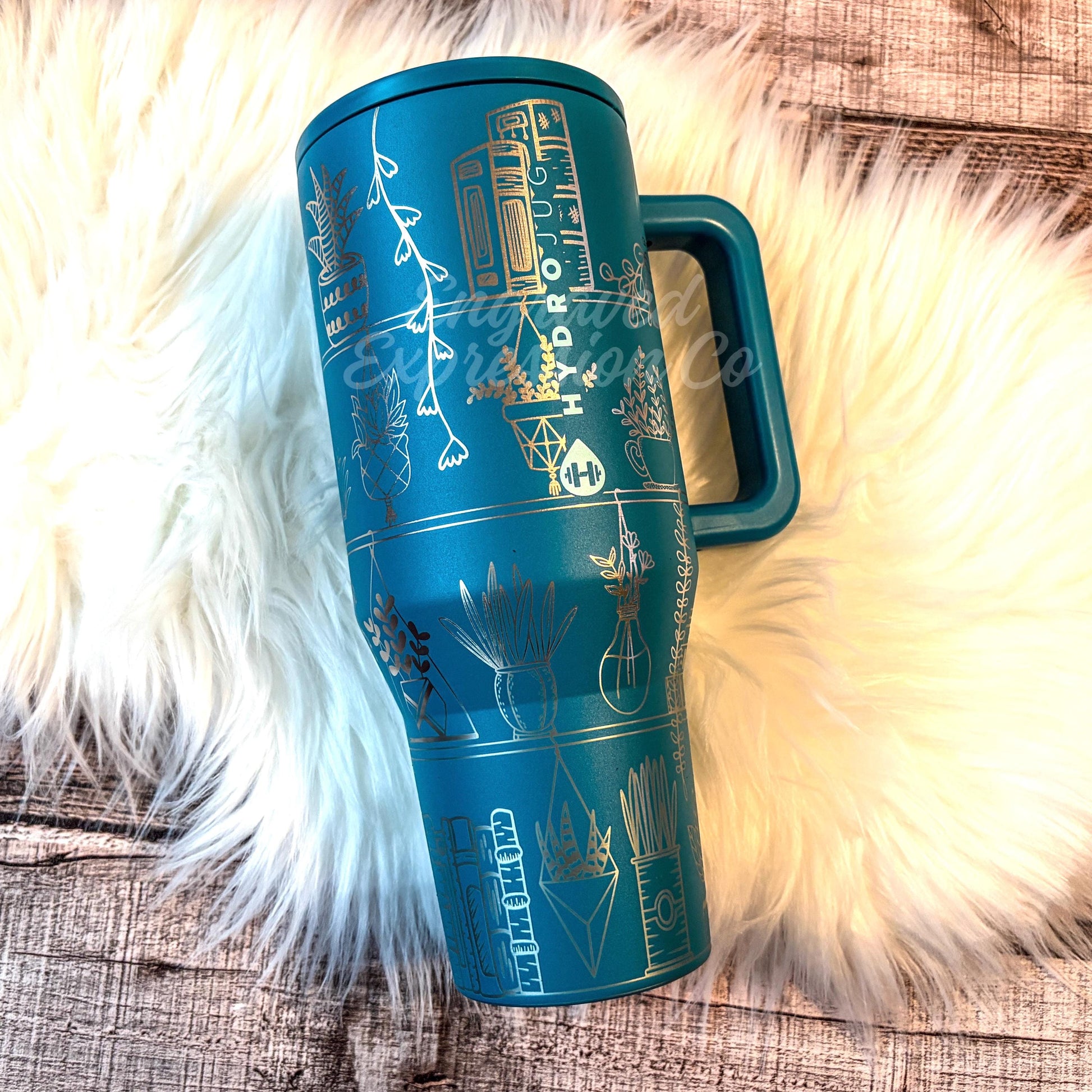 A blue insulated tumbler mug with various decorative designs and illustrations on it, placed on a white furry surface.