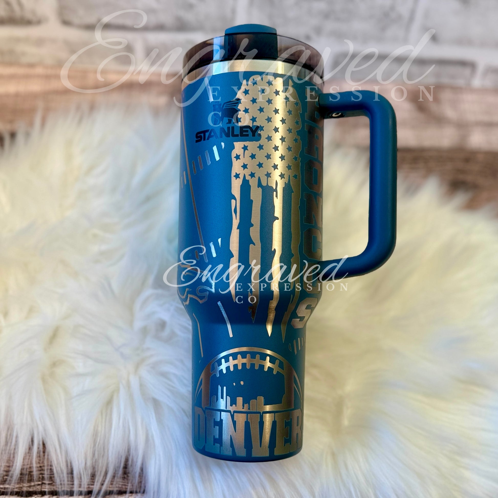 A blue Stanley sports thermos mug with a handle and a lid, featuring a design with a football and a city skyline.