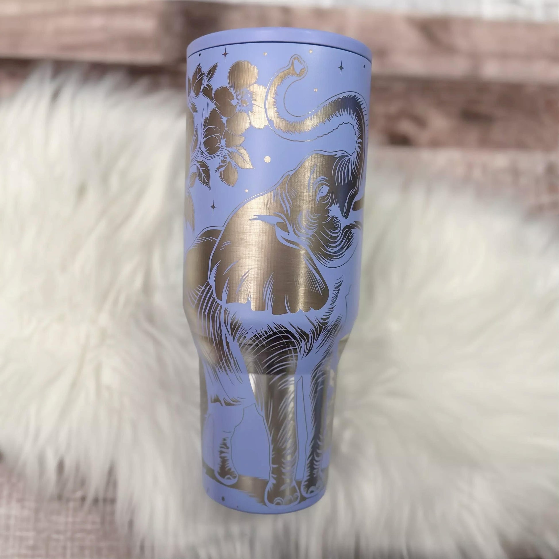 A purple insulated tumbler with a gold elephant design on it, placed on a white fur surface.