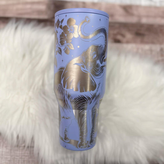 A purple insulated tumbler with a gold elephant design on it, placed on a white fur surface.