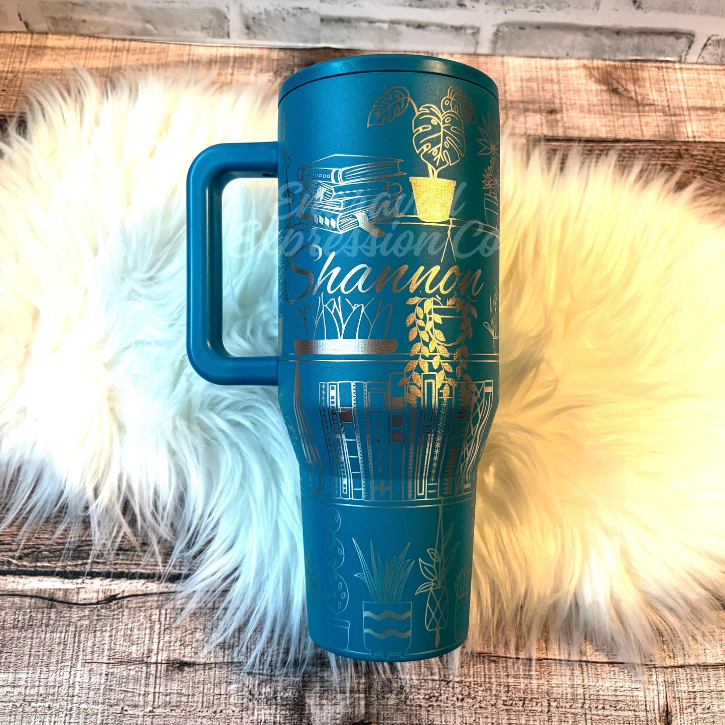 A blue insulated tumbler mug with a handle, placed on a white fur rug.