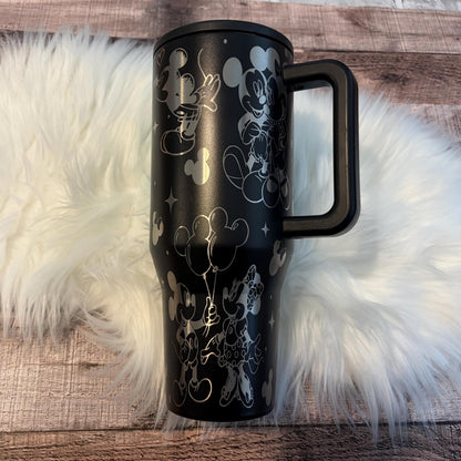 A black tumbler mug with a handle and a design featuring Mickey Mouse and Minnie Mouse characters.