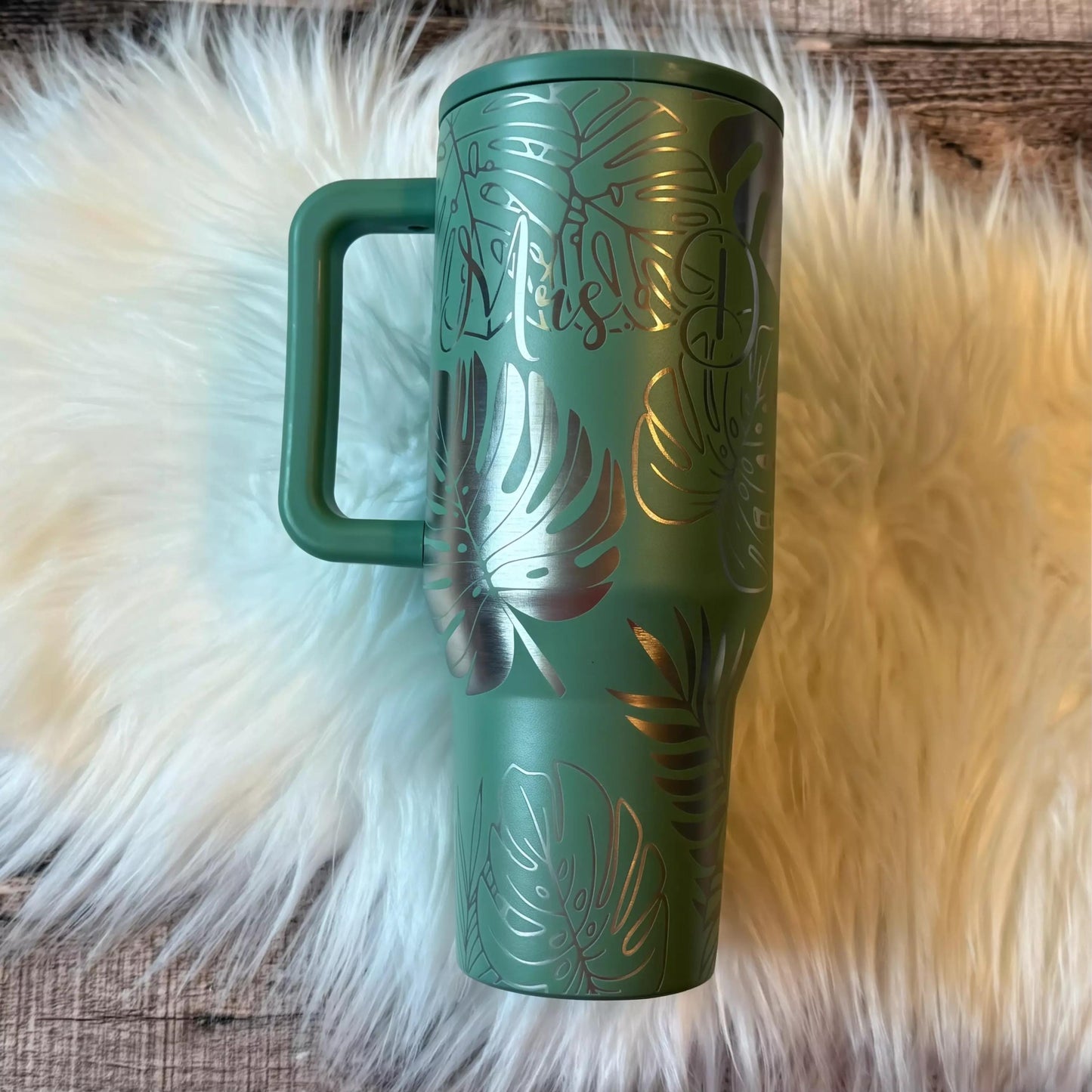 A green tumbler mug with a handle and a floral design on it, placed on a white furry surface.