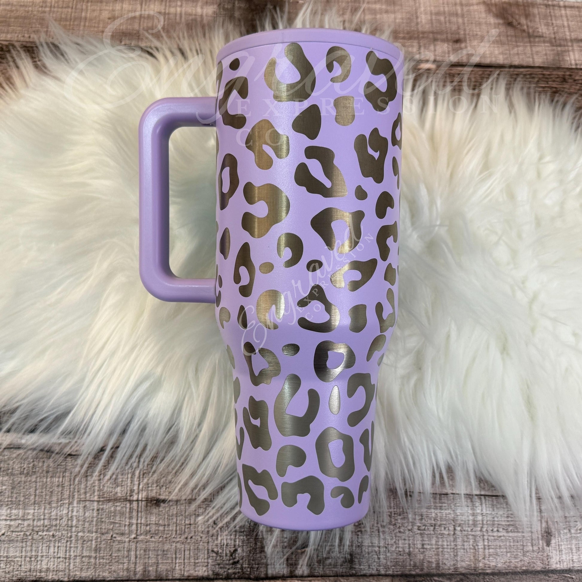 A purple insulated tumbler mug with a leopard print design is placed on a white furry surface.