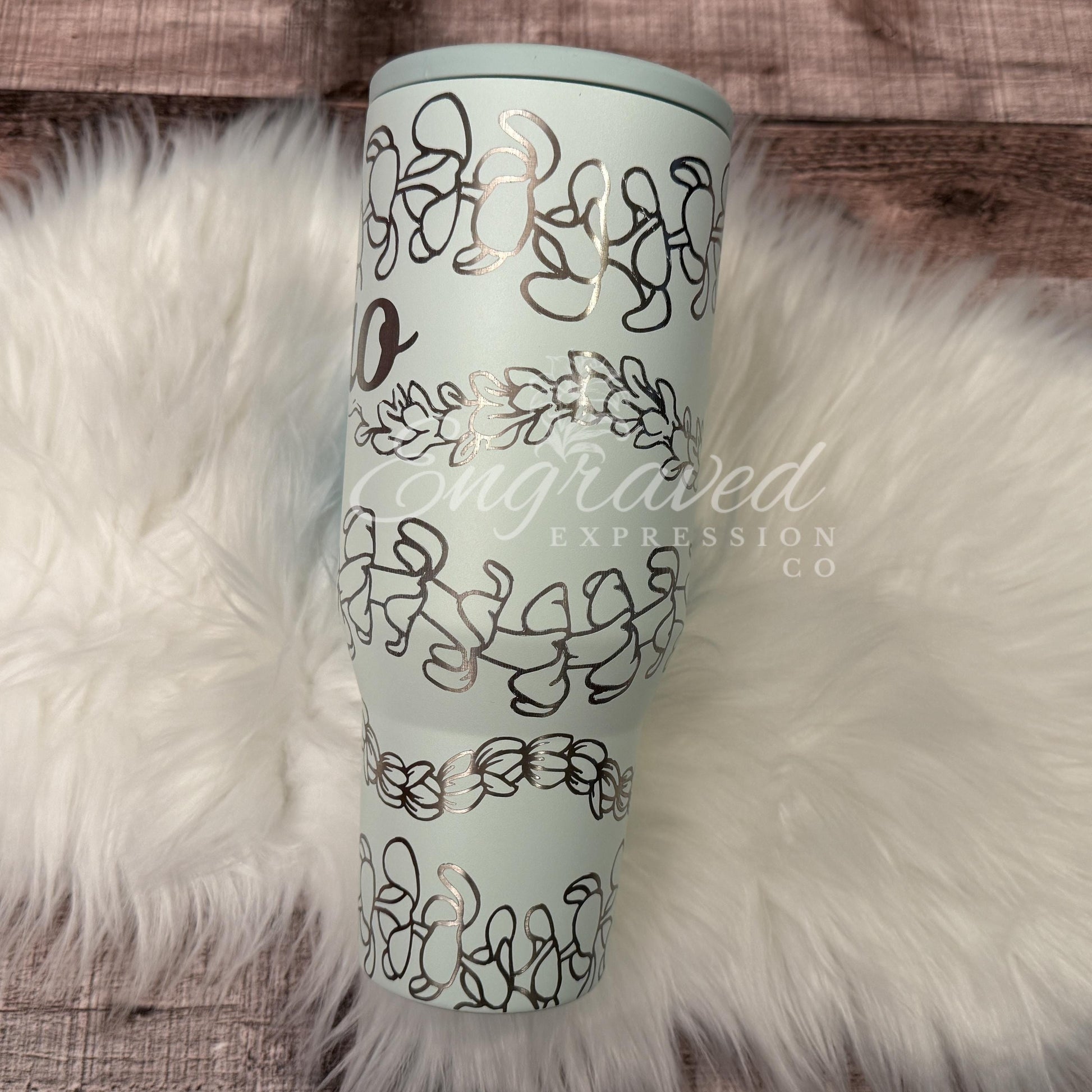 A turquoise tumbler with a floral design on it, placed on a white furry surface.